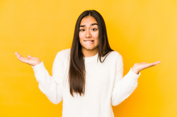 Young woman isolated on a yellow background confused and doubtful shrugging shoulders to hold a...