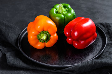 Green, orange and red bell peppers on a plate. Black background. Top view