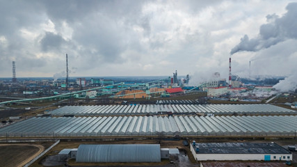Aerial view greenhouse on the background of smoke from the pipes of the pulp mill. Selective focus smoke from the chimneys. Ecological problem concept.