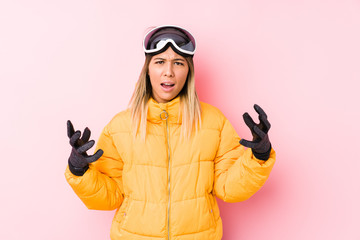 Young caucasian woman wearing a ski clothes in a pink background screaming with rage.