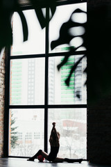 The gymnast sits on a twine and uses the ball. Silhouette of a girl on a bright window background.
