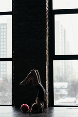 The girl does gymnastics with a red ball near the window. Silhouette on a bright background.