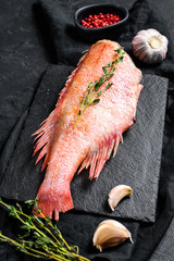 Raw red sea bass on a stone Board with thyme. Black background. Top view.