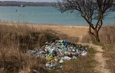 Garbage on beach of big city. People illegally throw garbage on seashore. Empty used dirty plastic...