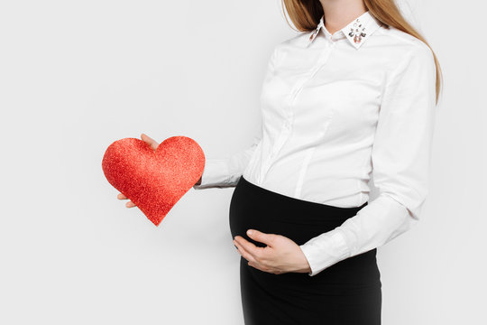Image of pregnant business lady hugging her belly, holding red heart near her belly
