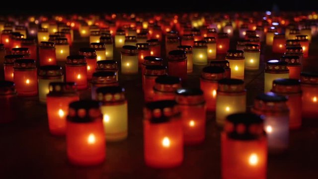 Many burning candles - concept of memory of the dead. Red round funeral burning candles. Candlelight in the dark. Laterns represent the memories of loved ones. Focus from foreground to background.