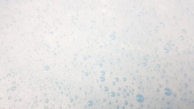 White foam with bubbles popping in blue water closeup