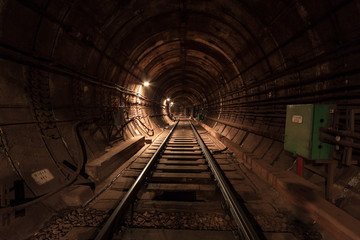 A lighted reinforced concrete subway tunnel, cable routes are laid, the railroad tracks turn left. In front of them are iron vertical boxes of automatics.