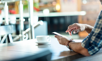 Man makes touch screen gesture with a smartphone in hand, at cafe. Closeup shot of abstract...