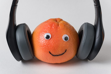 Orange with eyes and smile in headphones on white background. Food with Funny Faces. creative idea.