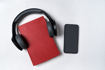 Mobile phone, book and headphones on a white background. Audiobook concept. Top view, copy space.