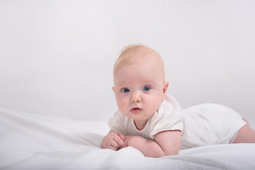 Funny little baby lying down on white blanket. Textile and bedding for kids.