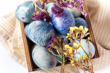 Easter colored eggs in a wooden box on white background. Easter eggs and spring flowers. Holiday pattern.