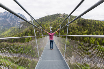 man on his back with arms raised crosses a suspension bridge