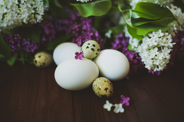 Chicken and quail eggs in a bouquet of lilac on a wooden table