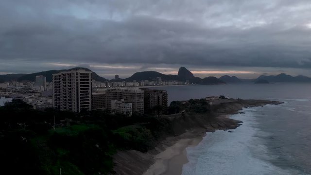 Early morning aerial tilt and ascend showing sunrise over Copacabana fort with the beach lights still on and Sugarloaf in the background in Rio de Janeiro, Brazil
