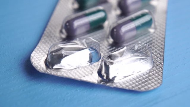 Blister pack of green purple medical capsules on a blue wooden table. Two capsules are missing. Medical concept. Macro shot. Hormonal contraception