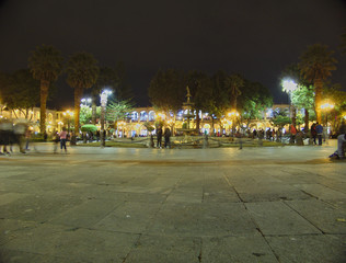 Arequipa's main square at night, illuminated with people walking in it.