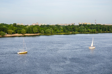 View on the top. Yachts on the river. Beautiful ship yachts with white sails in the Dnipro river on a background of the Kyiv city landscape. Ukraine