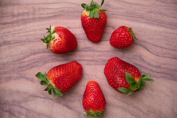Circle of strawberries on a veined light wooden background
