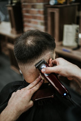 Good looking young adult man getting a hair and beard styling and dressing treatment by professional hairstylist.