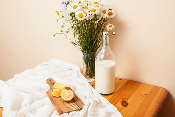 Simply stylish wooden kitchen with bottle of milk and glass on table, summer flowers camomile, healthy foog moring concept