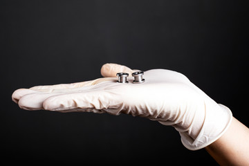 hand in a disposable white glove holds piercing tunnels on a dark background close-up. ear jewelry silver color