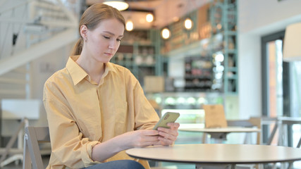 Serious Young Woman using Smartphone in Cafe