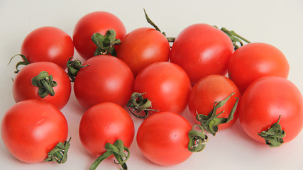 small red cherry tomatoes with green tails lie scattered on a white background