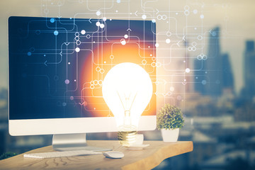 Computer on desktop in office with bulb icon hologram. Multi exposure. Concept of idea.