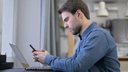 Young Man using Smartphone and Laptop