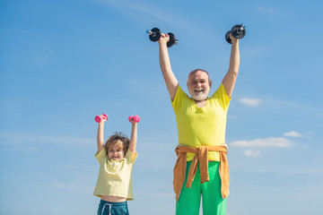 Grandfather and child is doing sport outdoors. Sport exercise for kids. Child raising a dumbbell....