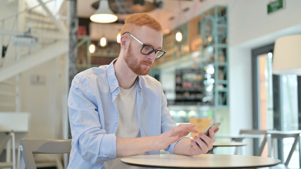 Naklejka na ściany i meble Focused Redhead Man using Smartphone in Cafe