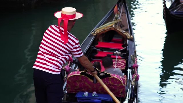 Gondolier navigating traditional gondola in Venice canal. Famous historic landmark in Italy. Summer tourism vacation & family travel destination in Europe. Slow motion. 