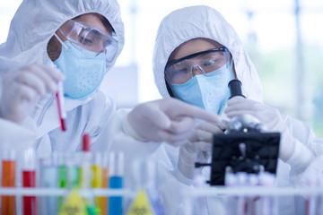 A female scientist wearing a mask and looking through the microscope in the laboratory, Concept, The scientists wear white protective clothing is experimenting with drug anti- Coronavirus, Covid2019