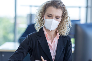 Business woman with curly blonde hair wearing a mask sitting in office, Concept,contagious disease, coronavirus, covid2019