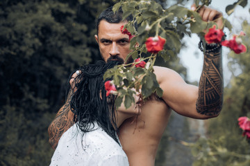 Sensual cople in love. Brutal bearded man holding rose ramification and embracing his beautiful...