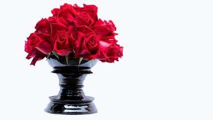Many red roses in a black vase that form a white back