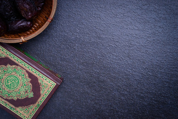 Eid Mubarak or Islamic concept. The Islamic holy book, Quran or Kuran, with dates (kurma) on grey background. Arabic words on the book means 