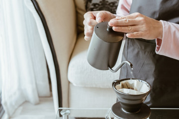 Cropped shot view of Barista hand pouring hot water on ground coffee with paper filter to make a drip coffee. Conceptual of how to making drip coffee by herself.