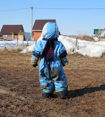 a small child boy stands in the mud with his back soiled clothes on a walk