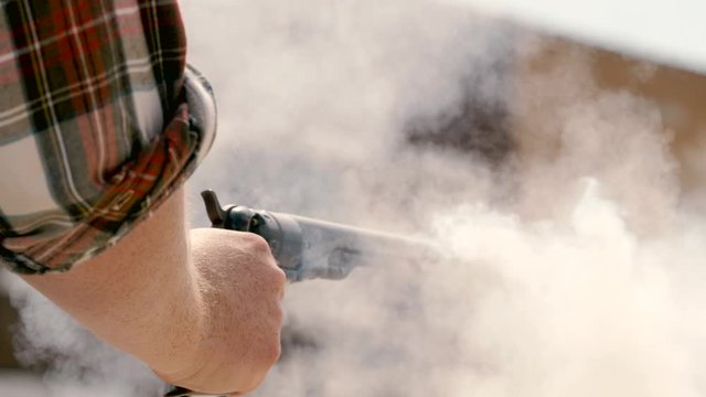 Close on cowboy shooting old gun enveloped in smoke at a shootout
