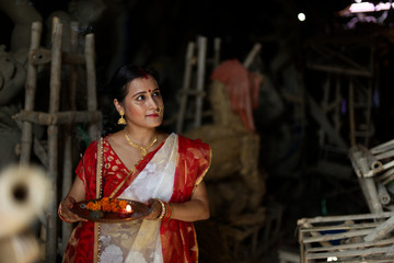 An young and beautiful Indian Bengali brunette woman in red white traditional ethnic sari holding a...