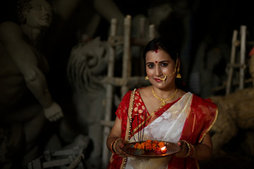 An young and beautiful Indian Bengali brunette woman in red white traditional ethnic sari holding a...
