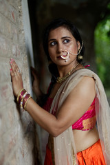 Portrait of an Young and beautiful Indian Bengali brunette woman standing while holding a brick wall wearing Indian traditional ethnic vibrant skirt blouse. Indian lifestyle and fashion