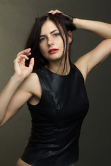 a brunette in a black leather sleeveless blouse poses on a gray background. warm toning
