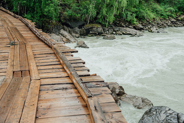 Wooden bridge of boards across mountain river. Rural old bridge in forest