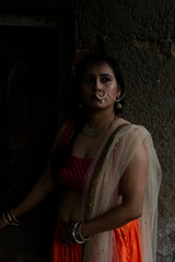 Young and attractive Indian Bengali brunette woman standing in front of a vintage house window wearing Indian traditional ethnic cloths pink and orange skirt blouse. Indian lifestyle and fashion