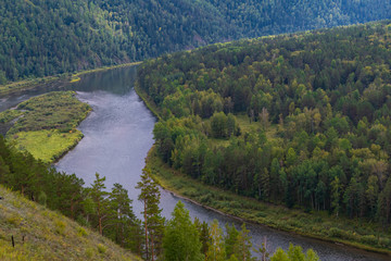 Fototapeta na wymiar wide river among green hills with trees, smooth bend of channel, forest on shore of reservoir, summer swimming and navigation