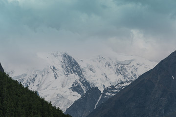 Fototapeta premium snowy mountain peaks on horizon of valley under clouds, travel to mountain area